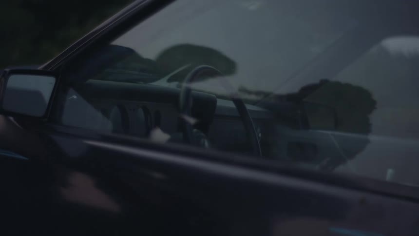 The reflection of a car window showing a woman pushing a man