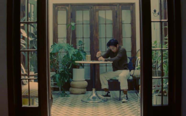 A man looking tired drinks from a mug and suddenly shakes his leg