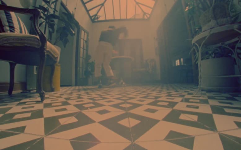 A young asian man doing a quick movement performance in a room with chairs and plants