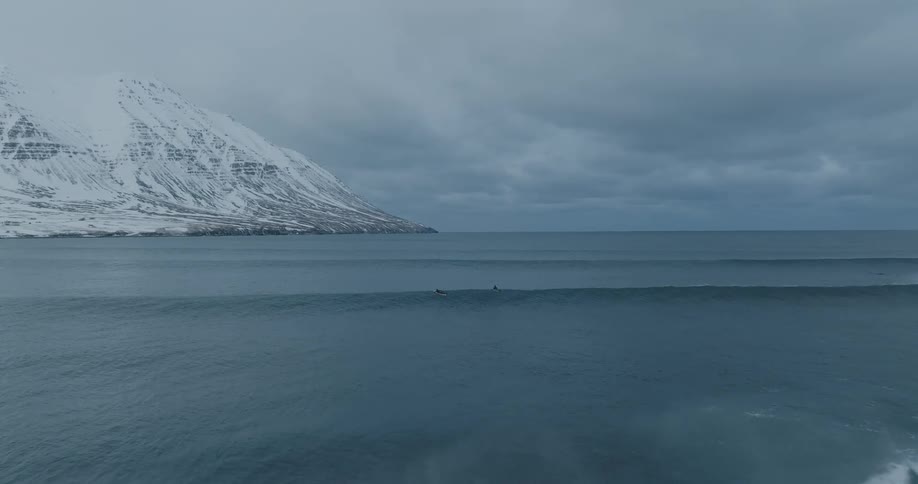 Surfers paddle out towards snow covered mountain