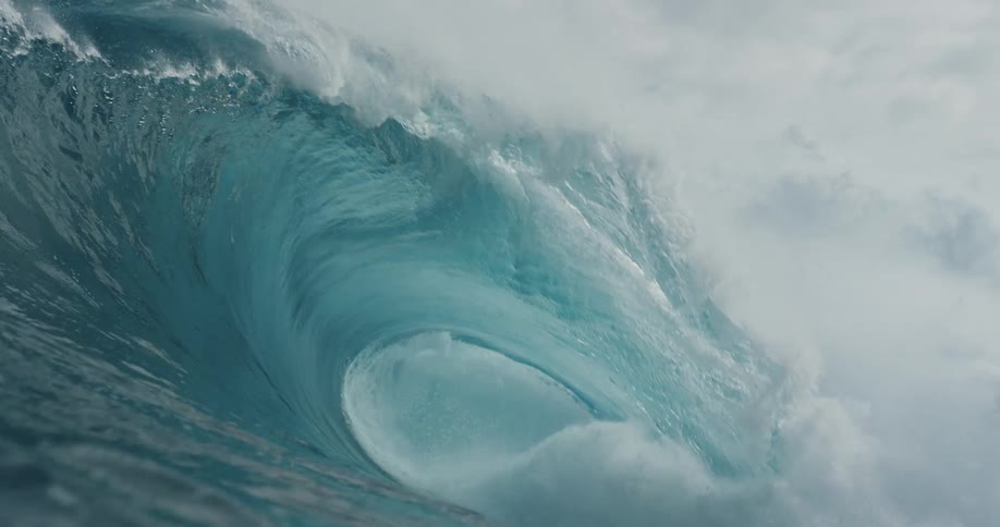 A big clear blue wave curls and splashes as it rolls into shore