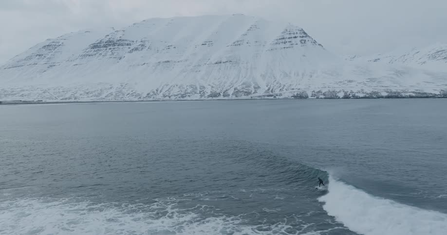 Person surfing at the sea near the coast with an icy mountain on the background during day time
