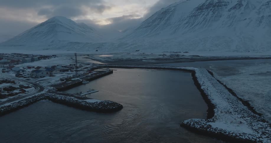 Water ripples in an icy river harbor with snow covered mountains on the coast