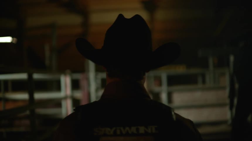 A man with a cowboy hat walks down a dark hall