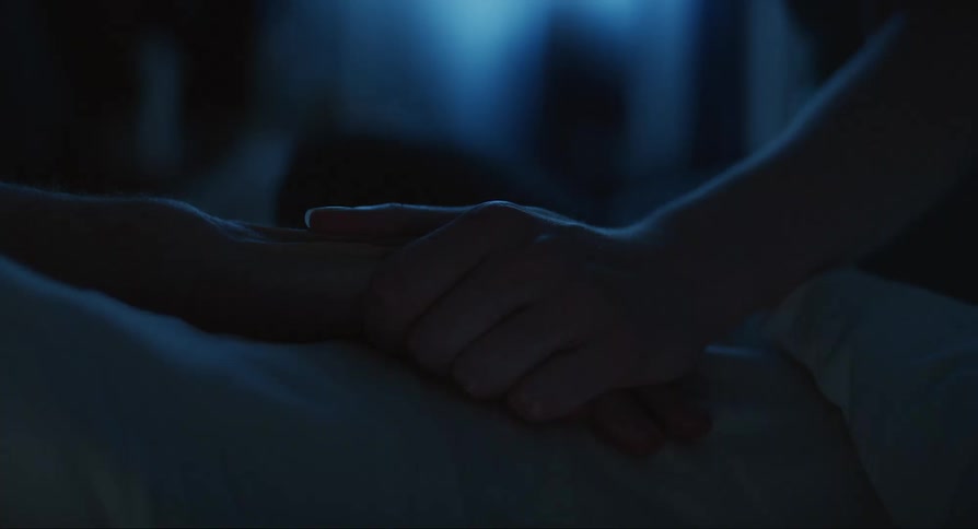 Closeup of an elderly person lying in bed while another person places their hand on the elderly persons hand
