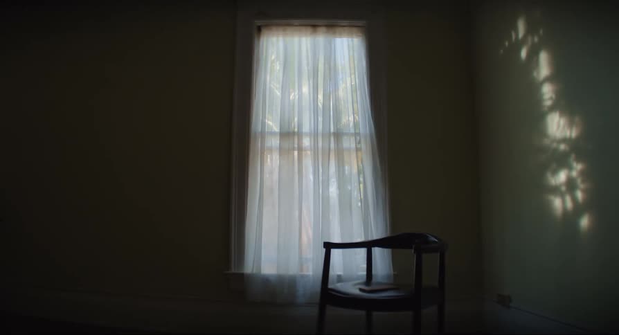 View of a room inside a house with a window adorned with a white curtain creating reflections on the wall