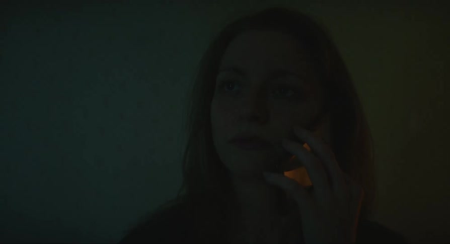 A woman sitting on the bed talking on her cellphone in a dark environment