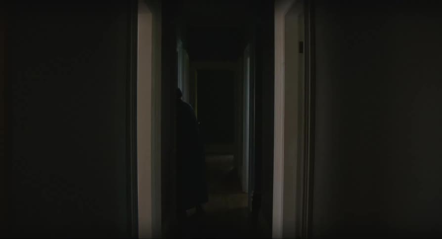 A person crosses a dark hallway from room to room