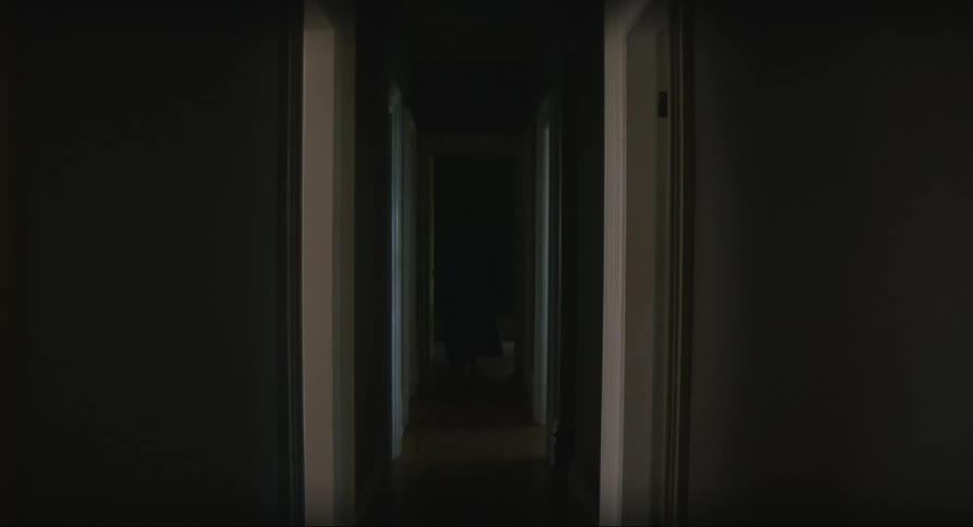 A person comes out of a door and walks down a dark hallway