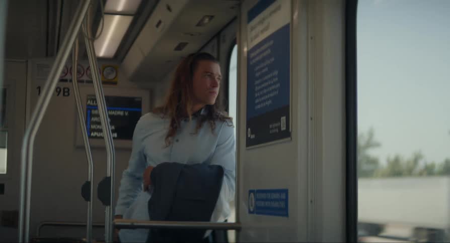 Man with long hair and light blue shirt travels by tram