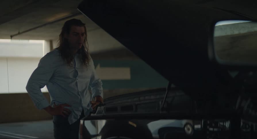 Man pacing near a faulty car with opened bonnet in a garage during the day