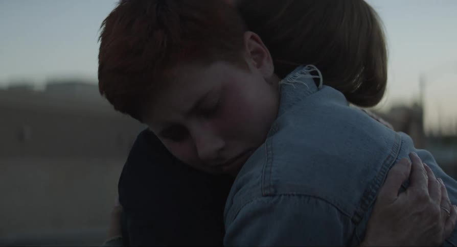 Two people walking up to each other in a parking lot grabbing each other in a hug looking sad