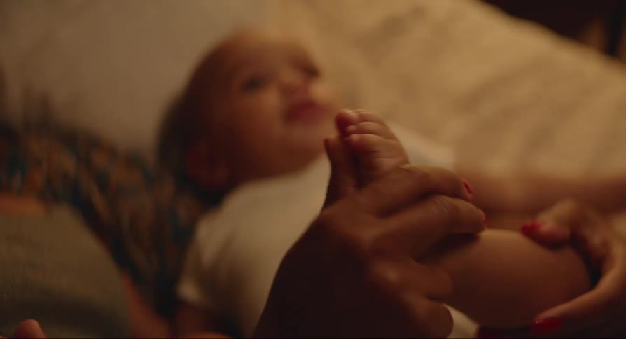 A baby lying in bed while a hand plays with their foot