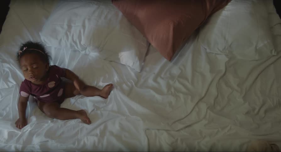 A baby girl sitting on a bed moves her arms