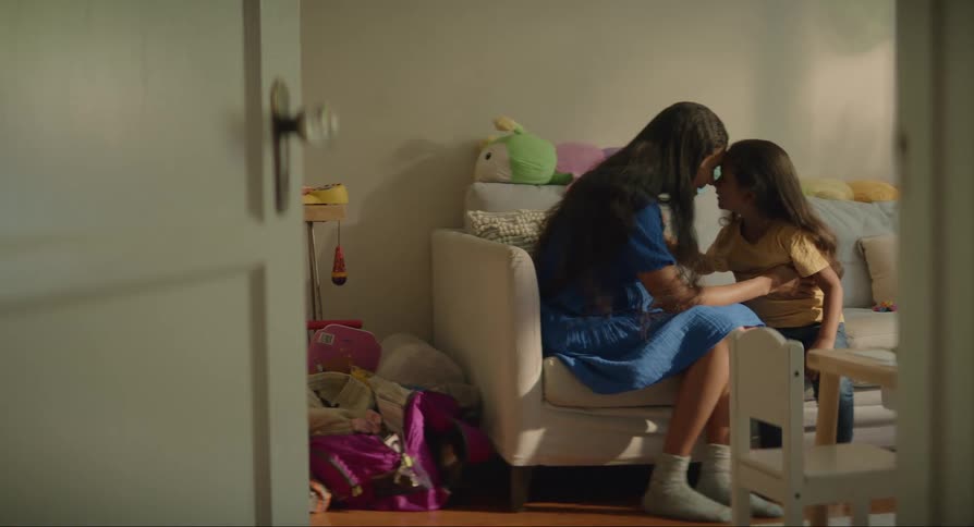 Mother and daughter sitting on a sofa gently touching their foreheads together in an affectionate manner