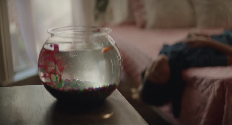 A teenage boy hangs off the side of his bed staring at his pet goldfish