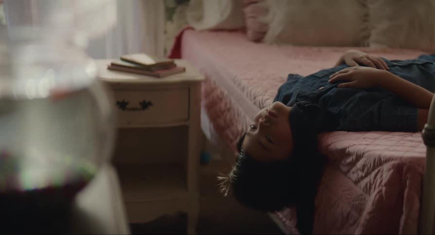 A teenage boy hangs off his bed as he stares at his pet goldfish