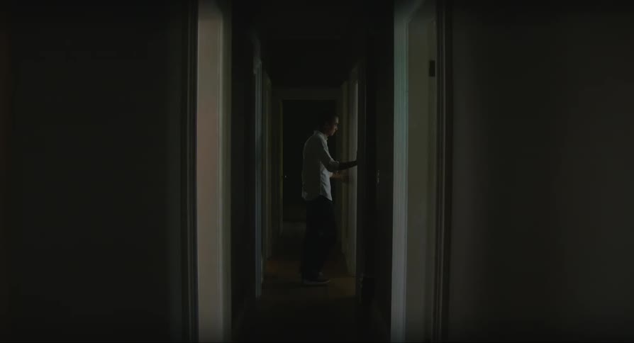 Man in white shirt and black pants stands in dark corridor