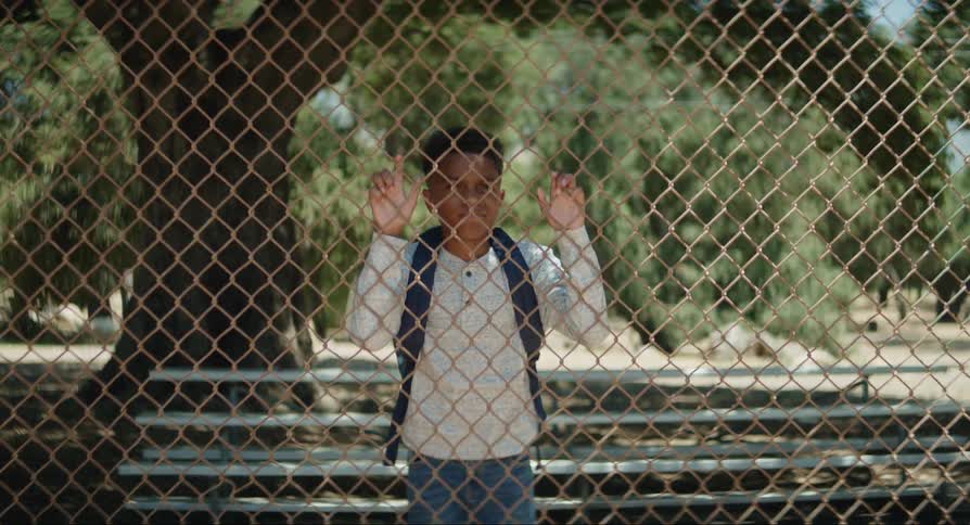 Boy wearing backpack walks toward chainlink fence