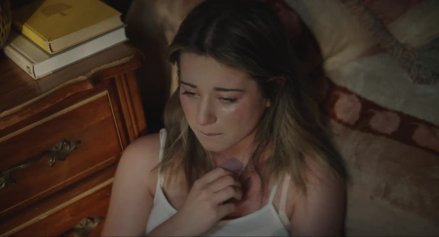 A young girl sitting on the side of her bed crying and looking at her cell phone