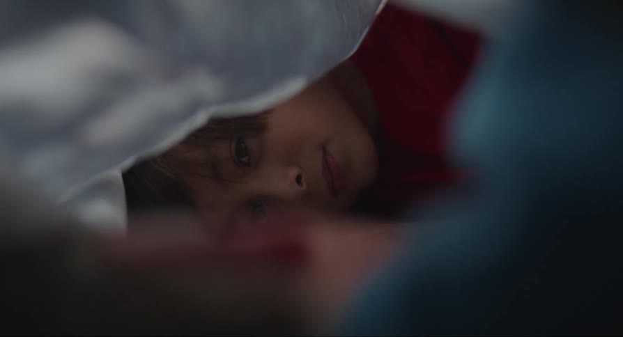 A boy lying under the white blanket is talking