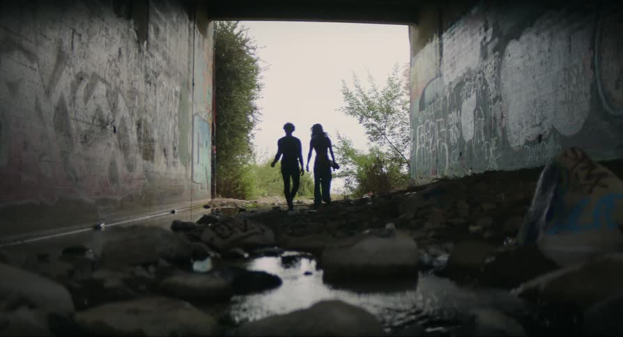 A boy and girl walking forward from underneath an abandoned structure