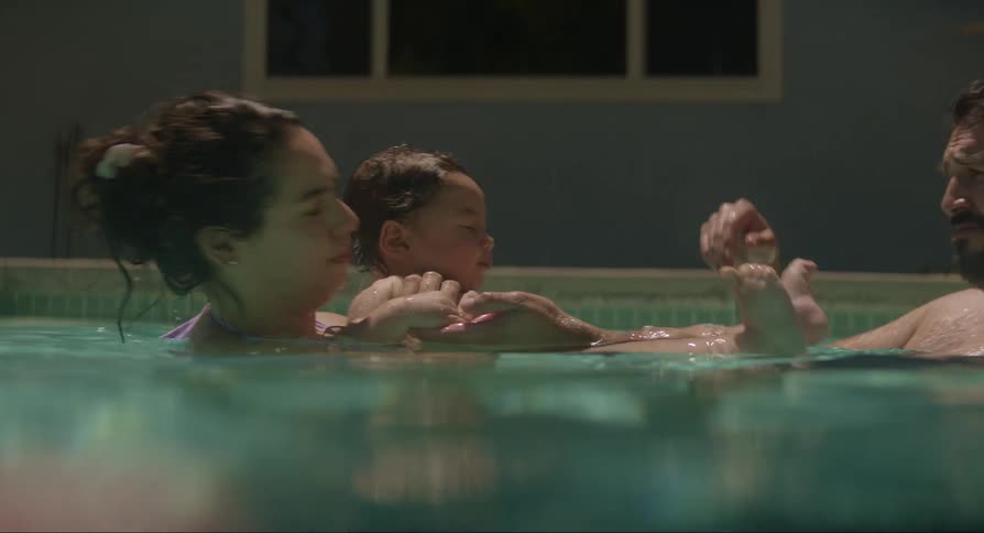 Young father and mother in a swimming pool playing with their baby outdoors during day time