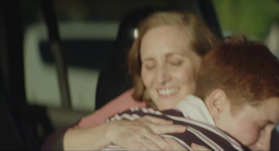 A woman hugs her teenage son inside the car and pats him on the back