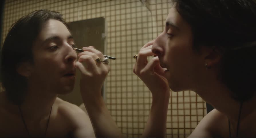 A young man at the mirror applying eyeliner on himself