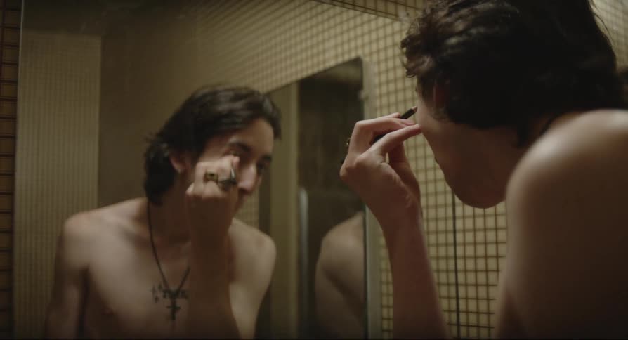 Close up of a young man putting makeup on his face in a bathroom mirror
