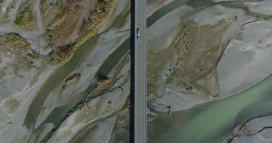 Aerial view of a road with a vehicle passing through an outdoor rocky environment with lakes