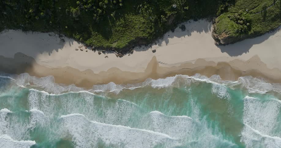 Topdown aerial of sea waves gently breaking on the coast of a beach