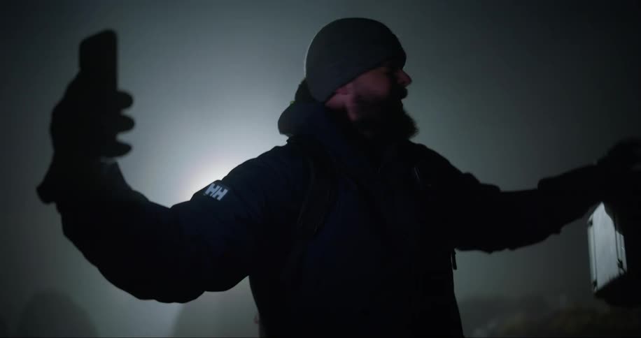A man wearing a winter hat and coat standing outside on a video call on his phone