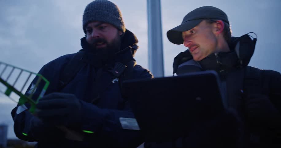 Two male workers manipulating electronic equipment and pointing to a specific location