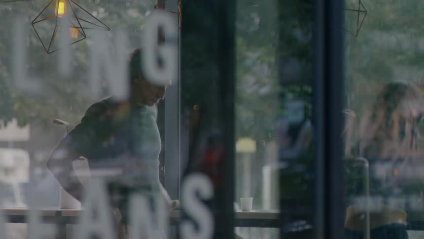 A man inside a cafe sitting at a bar before standing up and putting something in his bag
