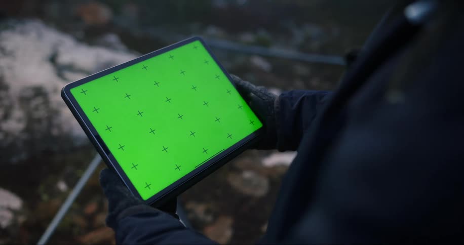 A man is standing outside holding a tablet computer with a green screen