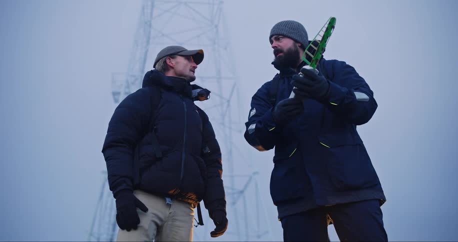 Two men talking over a device that is in the hand of one of them and one of them points in a direction