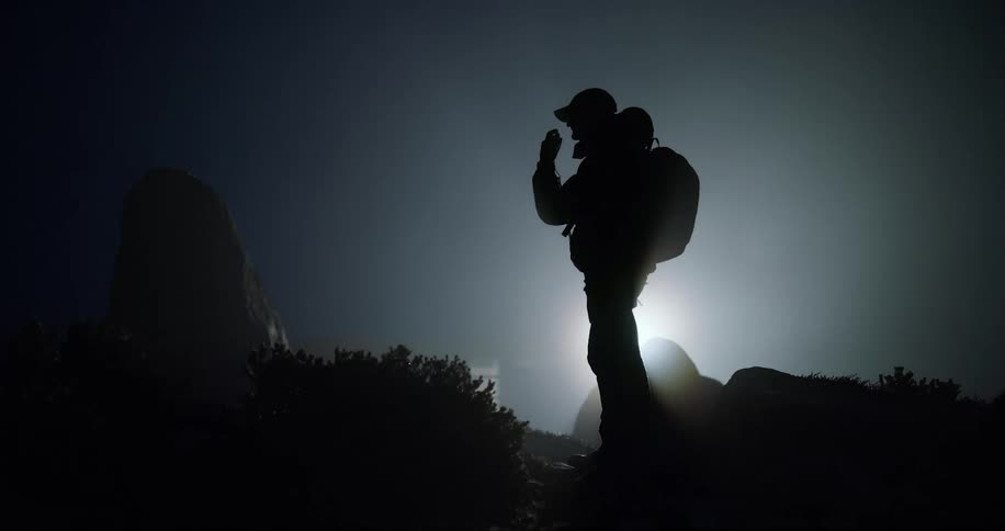 A silhouette of a person standing in front of a bright point of light and then he walks