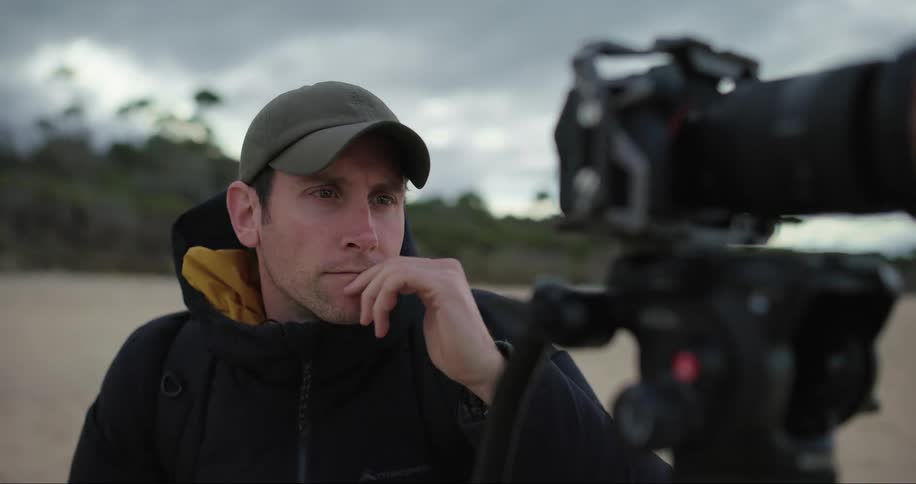 Close up of a male photographer setting up his camera on a beach during the day as he smiles