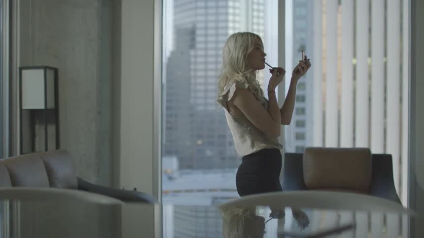 Woman applies makeup in an office while looking in a small mirror