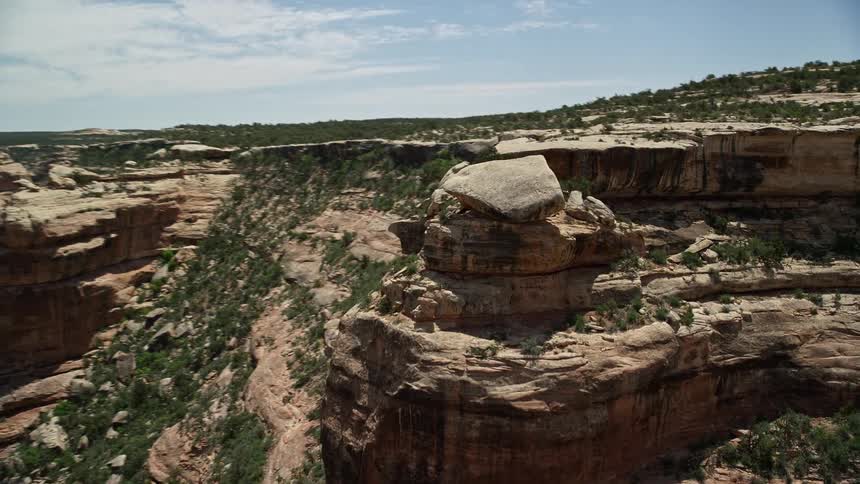Aerial footage of a giant boulder orbiting atop a canyon cliff in the arid and sunny Grand Gulch Primitive Area in Utah