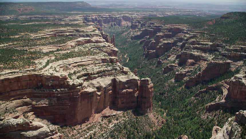 Aerial footage of Manti-LA Sal National Forest in Utah with a tilt up to reveal Arch Canyon amidst a lush green valley surrounded by rocky formations
