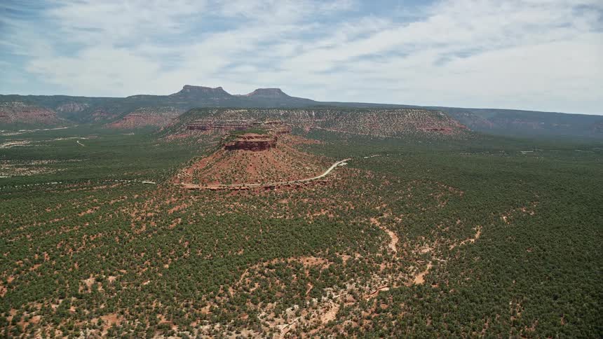 Aerial footage flying towards a butte and mesas with State Route 275 in Manti-La Sal National Forest Utah showcasing the natural beauty of the arid desert landscape