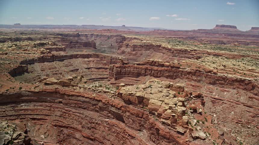 Aerial footage flying over the rock formations and Big Spring Canyon capturing the stunning natural beauty of Canyonlands National Park Utah with sunshine illuminating the arid landscape