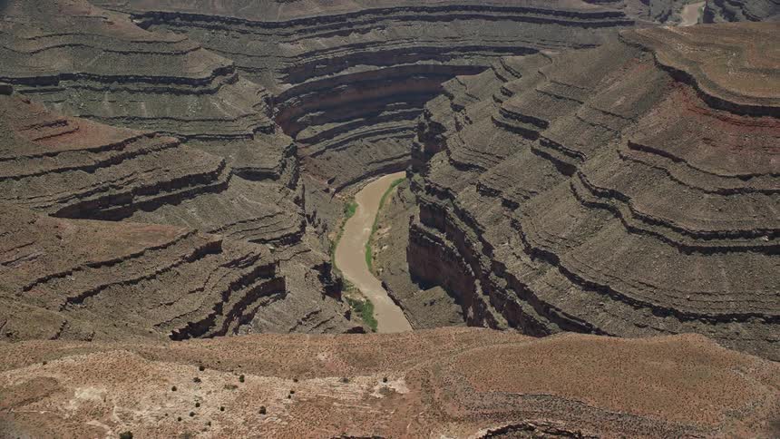 Aerial footage showcasing the stunning Rocky Mountain formations and a sand road situated in the deep canyon of the Navajo Nation Reservation in Utah and Arizona with the San Juan River flowing nearby