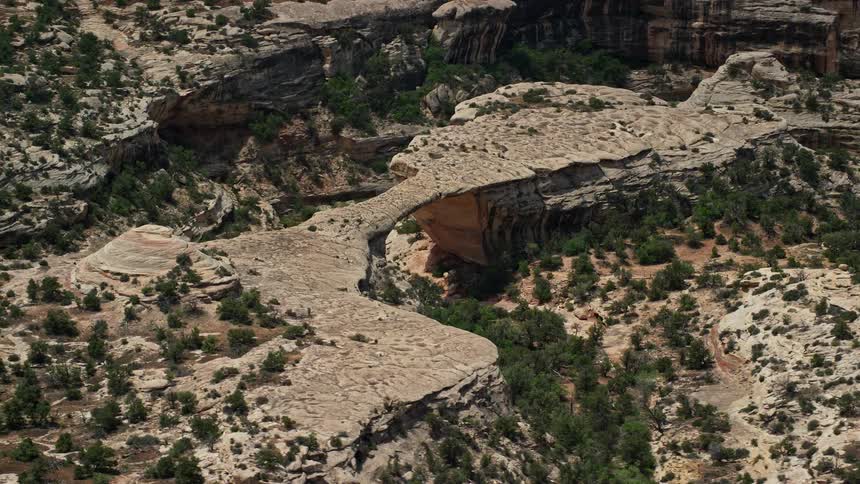 Aerial view of Owachomo Bridge a natural rock bridge in the badlands of Utah's Natural Bridges National Monument captured on a sunny day showcasing the arid canyon landscape and stunning rock formations