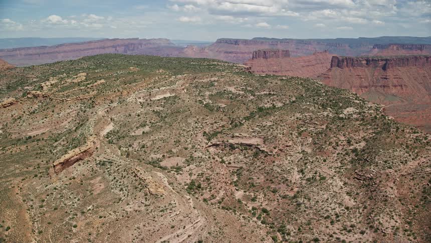  aerial footage flying over Dry Mesa in Moab Utah showcasing the arid desert landscape and flat topped mountain during a sunny day in summer