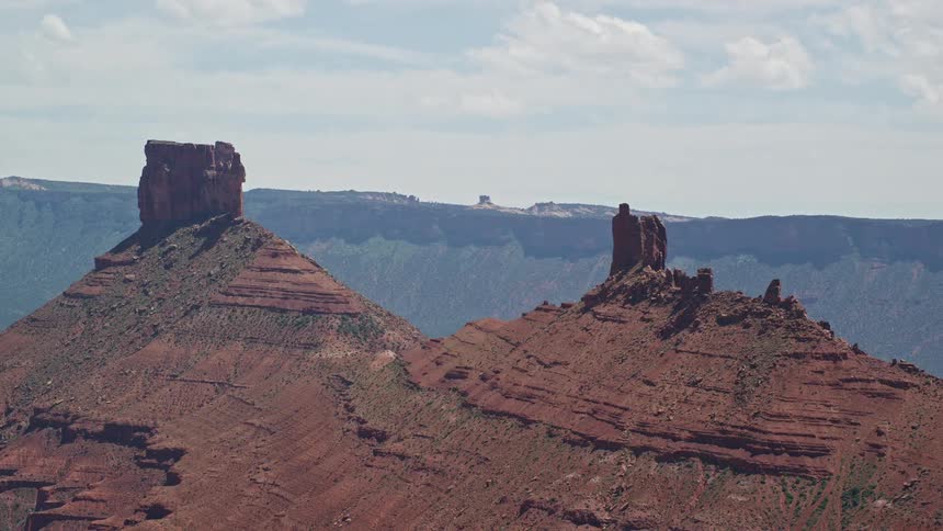 Aerial footage capturing the stunning rock formations and desert landscape of Moab Utah as the drone flies past two tall buttes in the sunny Southwest