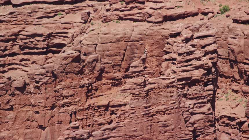 Aerial footage captures rock climbers orbiting a formation at Fisher Towers in Utah during a sunny day in the Southwest United States