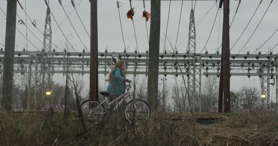 A girl pushes a bicycle on a cloudy day